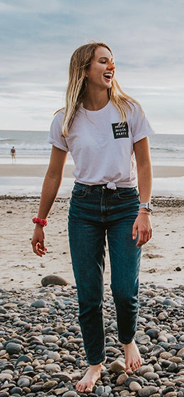 Woman standing and laughing as she walks on the beach with Nöz's orange sunscreen on her nose. 