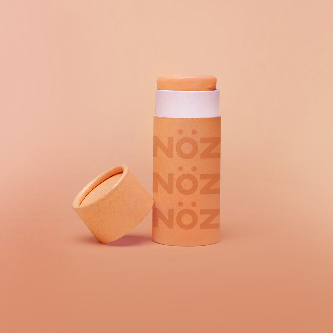 Nöz's orange sunscreen stick in front of a light orange background.