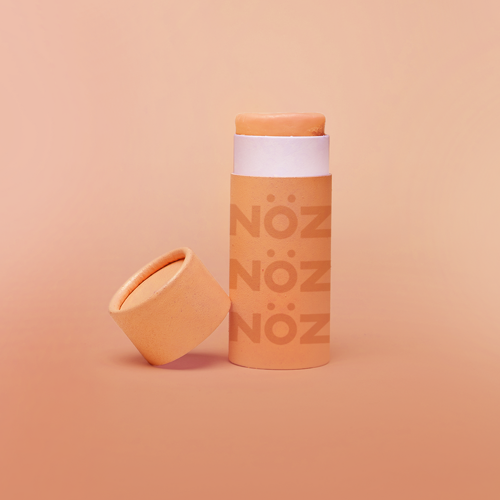 Nöz's orange sunscreen stick in front of a light orange background.