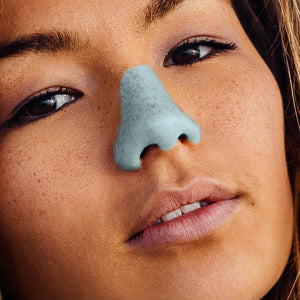 Close up of woman wearing the light blue variation of Nöz's sunscreen on her nose.